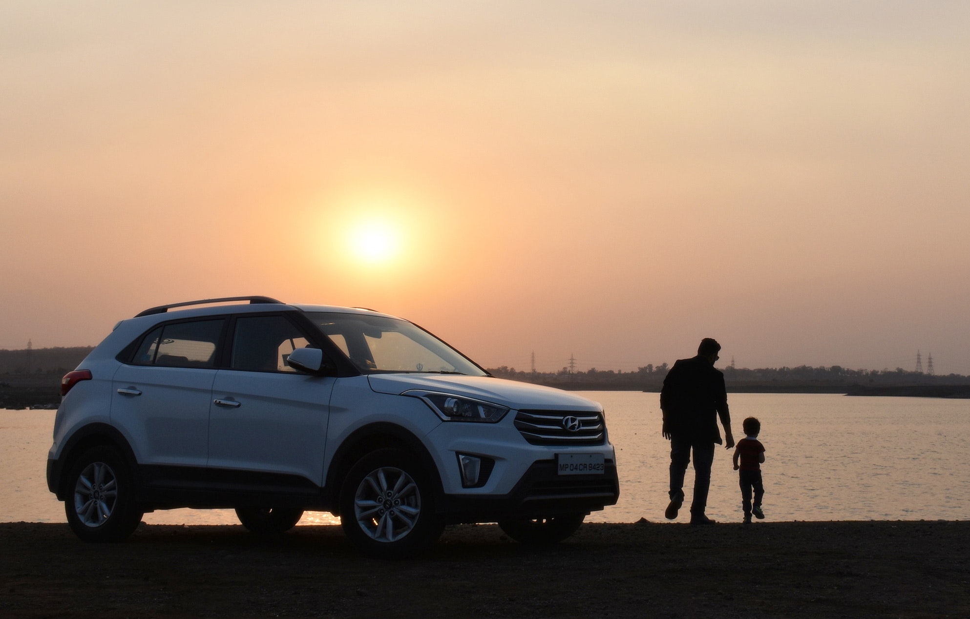SUV Hyundai blanc et père avec enfant au bord d’un lac au coucher du soleil